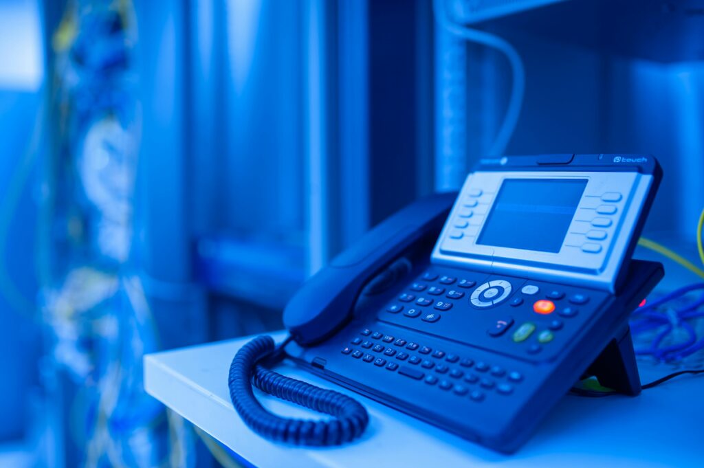 A unified communications VoIP phone on a desk with a blue hue